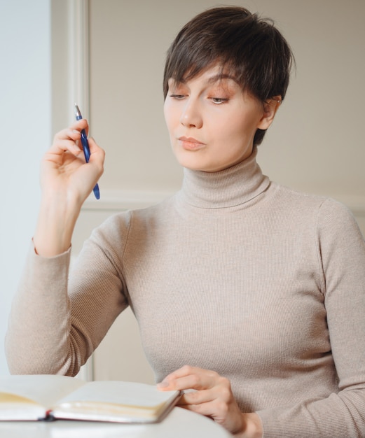 Attractive young woman with pen in hand thinking on plans and writing list to do in notepad enjoying recreation time in stylish cafe