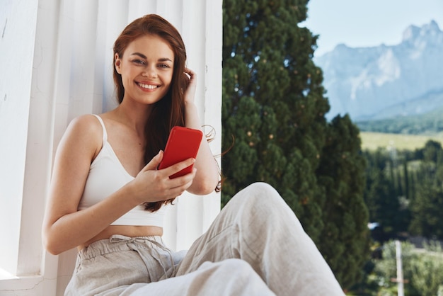 Attractive young woman with a red phone terrace outdoor luxury\
landscape leisure unaltered
