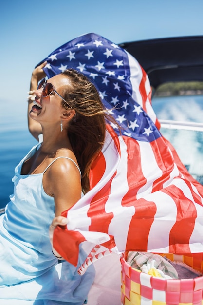 Giovane donna attraente con la bandiera nazionale degli stati uniti divertendosi e trascorrendo la giornata sul suo yacht privato.