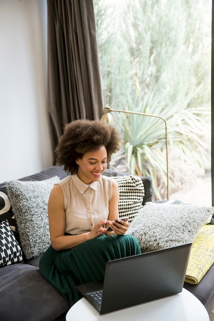Привлекательная молодая женщина работает на ноутбуке и с помощью мобильного телефона в домашних условиях