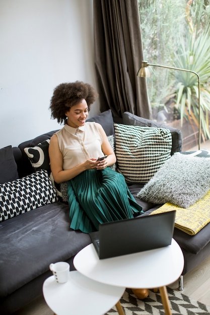 Attractive young woman working on laptop and using mobile phone at home