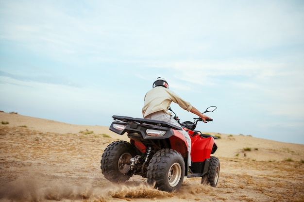 砂漠でレースをするATVライダー、砂漠の砂浜でのダウンヒルライディング、アクションビュー。クワッドバイク、砂のレース、暑い晴れた日の砂丘サファリ、4x4の極端な冒険、クワッドバイクの男性