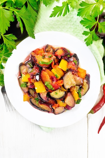 Aubergine gebakken met pruimen, uien en paprika's in een bord op een handdoek tegen de achtergrond van een houten plank van bovenaf