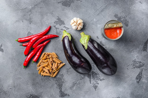 Aubergine penne ingredients eggplant pasta, pepper tomatoe sauce, on grey background top view.