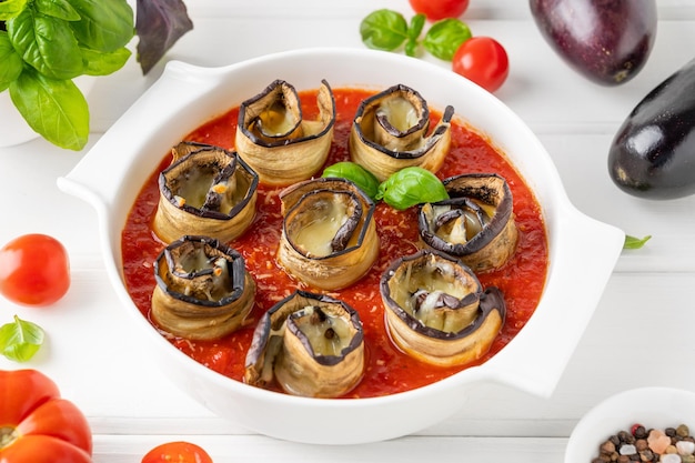 Foto aubergine rollen met kaas in tomatensous in een witte keramische bakvorm vegetarisch gezond gerecht