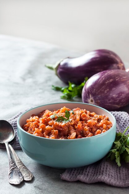 Auberginekaviaar in blauwe kom en verse groenten op achtergrond. Ruimte kopiëren