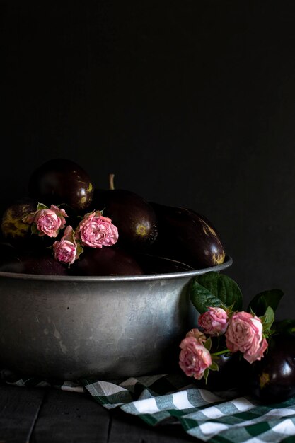 Aubergines en roze rozen in metalen kom met geruite groene en witte handdoek op zwarte achtergrond