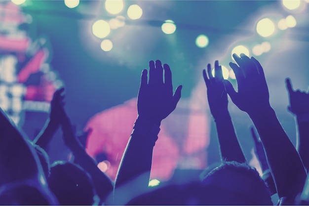 Audience with hands raised at a music festival and lights streaming