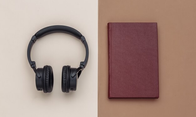 Audio book. Headphones and a book on brown beige background. Top view.