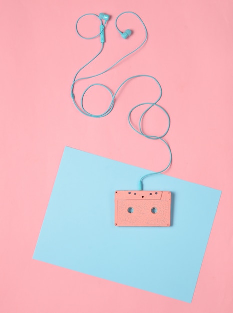 Audio cassette and earphones on a blue pink pastel background. Musical concept. Retro style. Minimalism. Top View
