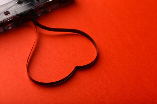 Audio cassette with magnetic tape in shape of heart on red background