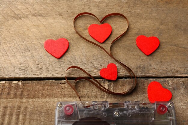 Audio cassette with magnetic tape in shape of heart on wooden background