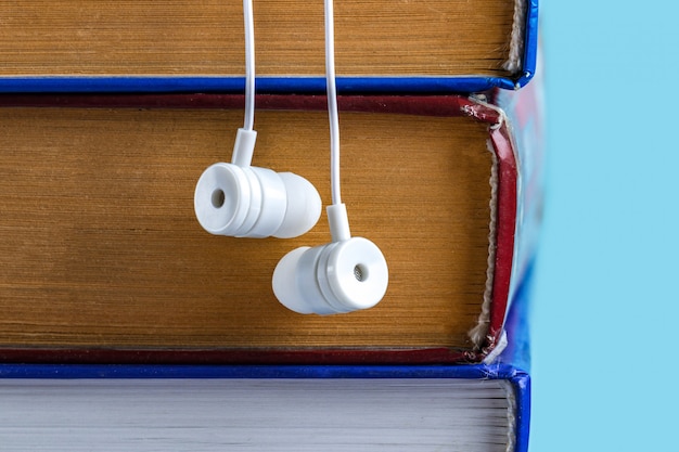 Audioboek concept. Een witte koptelefoon en boeken. Boeken lezen zonder op te kijken van het werk