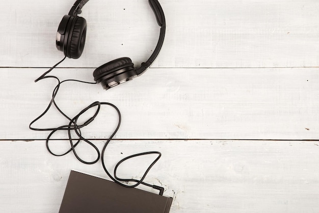 Audioboekconcept met zwart boek en hoofdtelefoons op witte houten achtergrond