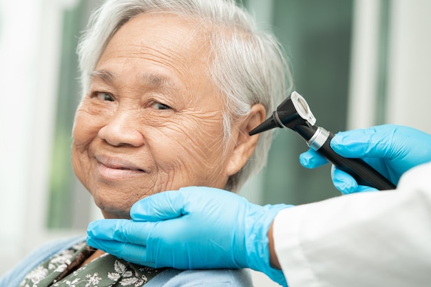 Audiologist or ENT doctor use otoscope checking ear of asian senior woman patient