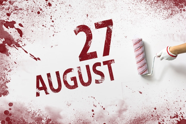 August 27th. day 27 of month, calendar date. the hand holds a
roller with red paint and writes a calendar date on a white
background. summer month, day of the year concept.