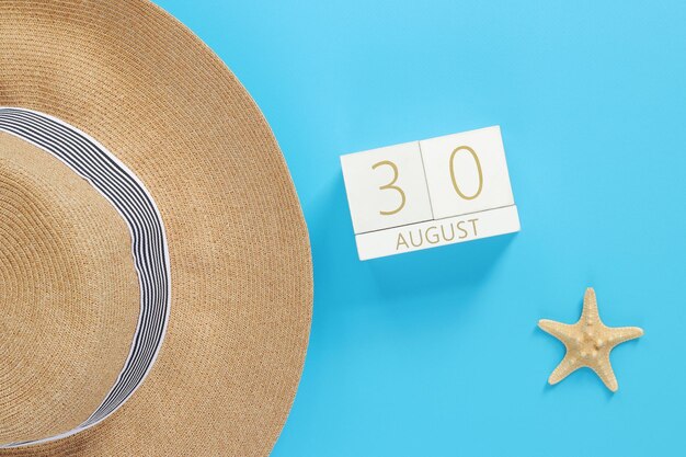 August Wooden calendar on a blue background with summer accessories top view Vacation 30