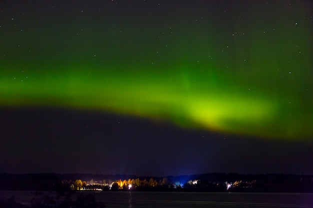 Aurora borealis over the city on the coast. Polar lights in the night starry sky over the lake.