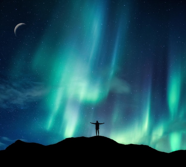 Aurora borealis gloeit over silhouet wandelaar staande op de berg in de nachtelijke hemel