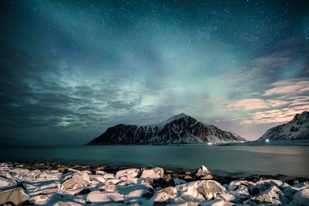 Aurora borealis met sterren over bergketen met besneeuwde kustlijn