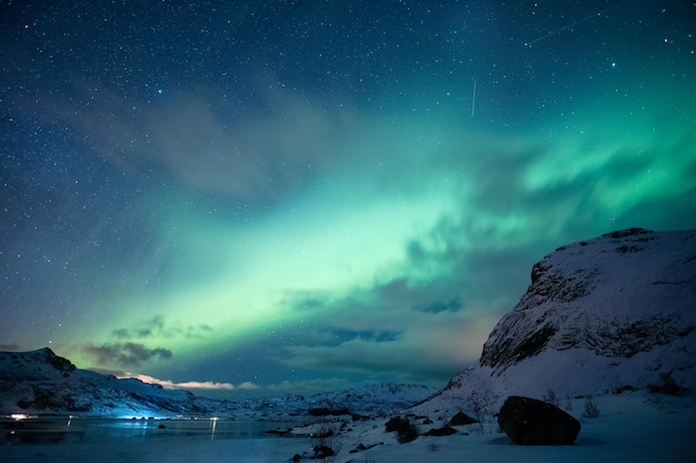 오로라 보레아리스 (Aurora Borealis) 북쪽 빛은 로포텐 섬의 북극 해의 눈 인 산 위에서 빛나고 있습니다.