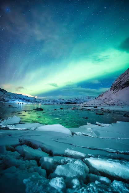 Aurora borealis Northern lights glowing over snowy mountain on arctic ocean at Lofoten Islands