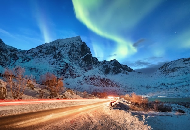 Aurora borealis op de Lofoten-eilanden Noorwegen Wegverkeer en vervagen autolicht Groen noorderlicht boven bergen Nachtelijke hemel met poollicht Natuurlijke achtergrond in Noorwegen