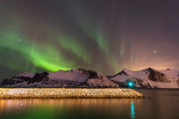 エルスフィヨルドビーチの桟橋と山の上のオーロラ。夜のセンジャ島。ノルウェー