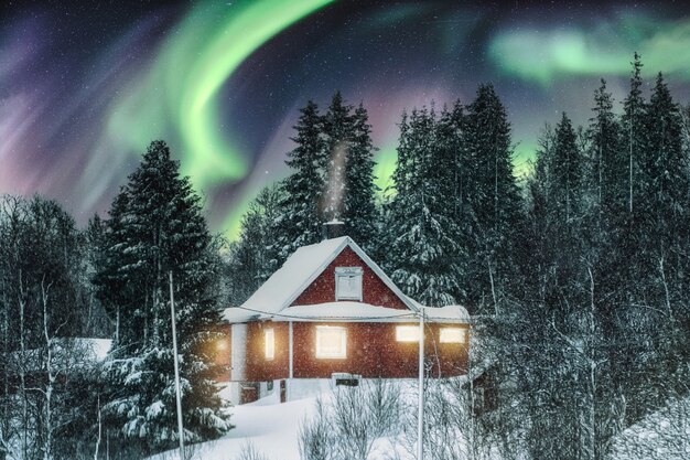 Aurora boreale sopra casa nordica rossa con neve in inverno in scandinavia