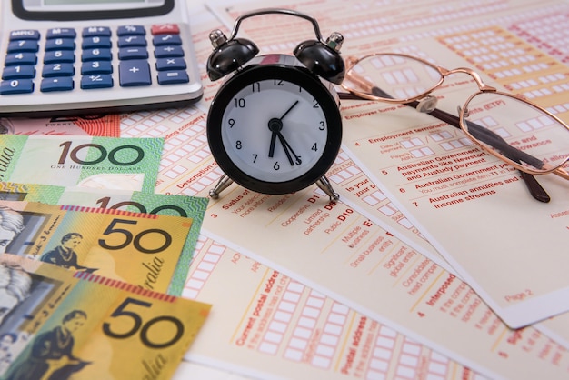 Dollari australiani, orologio e calcolatrice sul modulo fiscale
