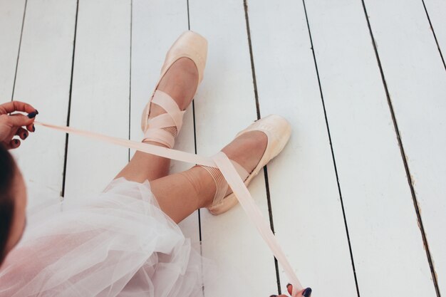 The authentic ballerina ballet dancer sitting on the floor and tying pointe shoes