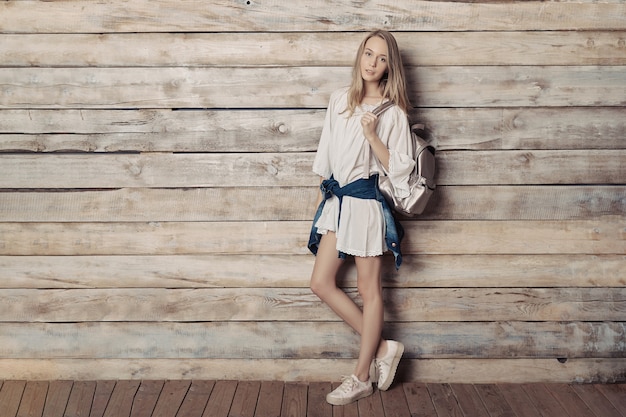 Authentic blonde young girl with silver backpack over wood wall