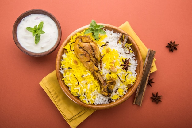 Authentic Chicken Biryani served in a bowl or plate over colourful or wooden background. It's a delicious recipe of Basmati rice mixed with spicy marinated chicken served with salad. Selective focus