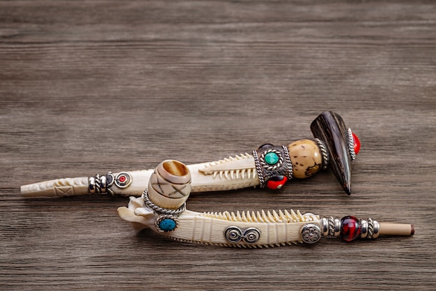 Authentic inlaid pipe for tobacco made of bone, on wooden background. Solemn pipe of Native American. Copy space.