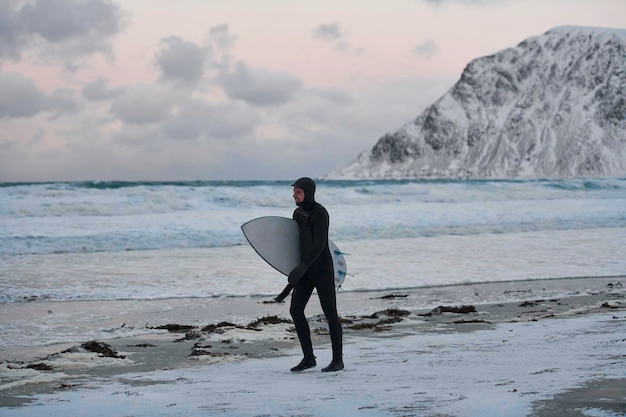 Authentic local Arctic surfer going by beach after surfing in Northern sea. Norwegian sea coastline. Winter water activities extreme sport