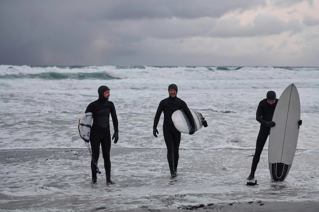 Authentic local Arctic surfers going by snowy beach after surfing in Northern sea. Norwegian sea coastline. Winter water activities extreme sport