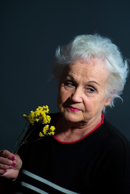 Authentic portrait of grandmother holding yellow flower on dark gray background