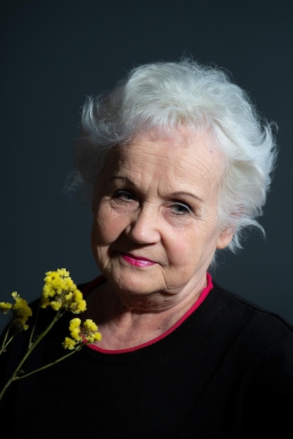 Authentic portrait of grandmother holding yellow flower on dark gray background