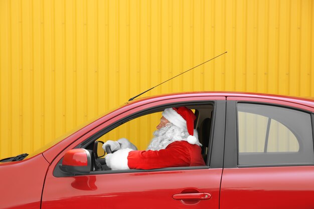 Photo authentic santa claus driving his red car against yellow background