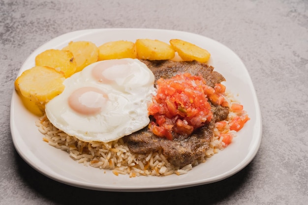 Authentic traditional Bolivian meal Silpancho made of beef potatoes rice fried eggs tomato an