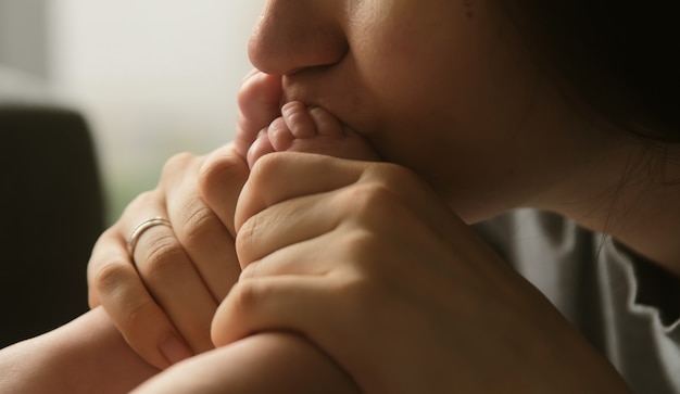 Authentic young mother gently kissing little feet of newborn baby child