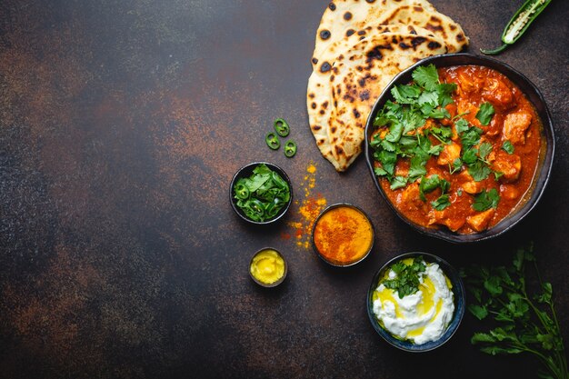 Authentiek Indiaas gerecht Kip tikka masala met ruimte voor tekst. Pittig kerrievlees in kom met vers brood Naan, yoghurtraitasaus op rustieke donkere achtergrond, bovenaanzicht, close-up, kopieer ruimte