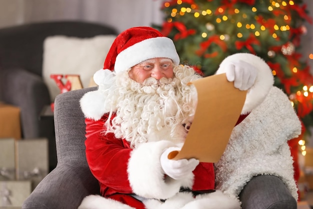 Authentieke kerstman met vel papier zittend in fauteuil in kamer ingericht voor Kerstmis
