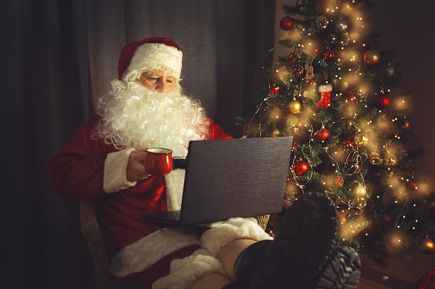 Authentieke Kerstman werkt op een laptop. Huis interieur. In afwachting van Kerst en Oud en Nieuw.