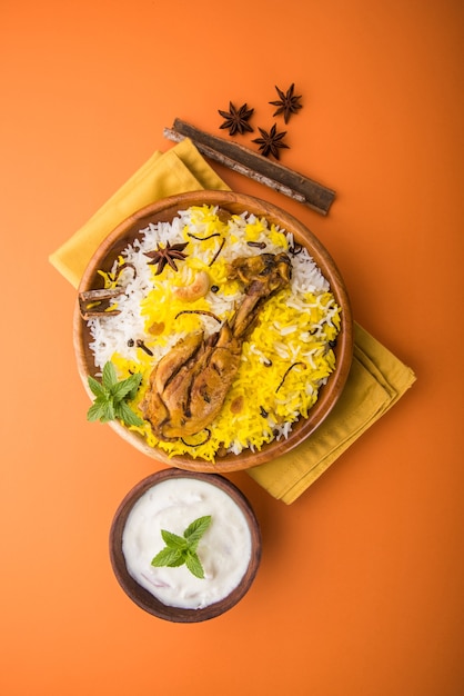 Authentieke Kip Biryani geserveerd in een kom of bord op kleurrijke of houten achtergrond. Het is een heerlijk recept van Basmati rijst gemengd met pittig gemarineerde kip geserveerd met salade. Selectieve focus