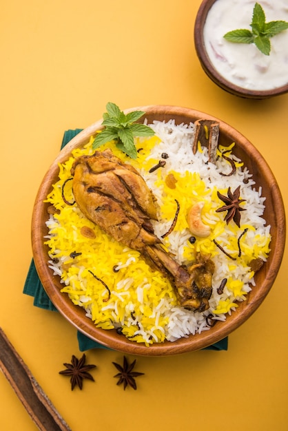 Authentieke Kip Biryani geserveerd in een kom of bord op kleurrijke of houten achtergrond. Het is een heerlijk recept van Basmati rijst gemengd met pittig gemarineerde kip geserveerd met salade. Selectieve focus