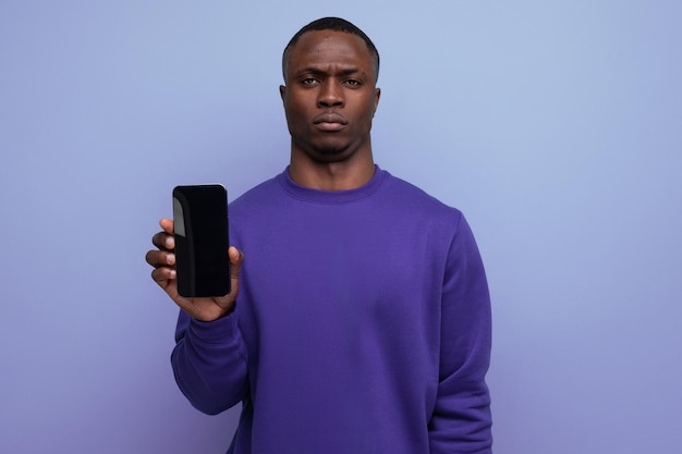 Foto authentieke knappe jonge afrikaanse man in blauwe trui die smartphone verticaal vasthoudt met mockup voor