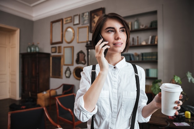 Authoress in white shirt talking on phone and holding cup of coffee