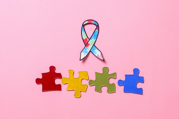 Autism awareness ribbon and colorful pieces of puzzle isolated on pink background World Autism Awar