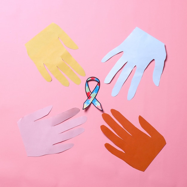 Autisme bewustzijn lint omringd door papier handen vorm geïsoleerd op roze achtergrond symbool van suppo